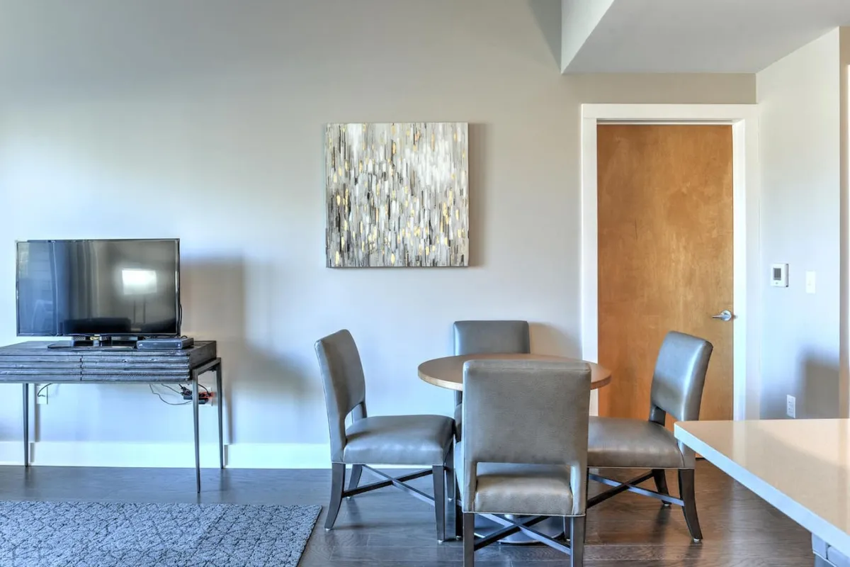This image captures a warm and inviting living and dining area with a comfortable table set for meals, a television for entertainment, and an eye-catching piece of art on the wall. The space feels open and communal, ideal for relaxing or socializing after a day out with your pet.
