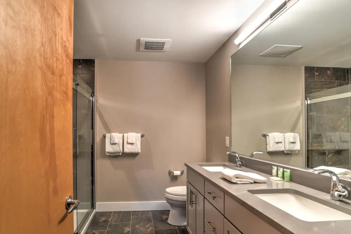 A modern bathroom with a sleek sink area, large mirror, glass shower stall, and plush towels. The tranquil color palette and spa-like touches set a refreshing and relaxing mood.