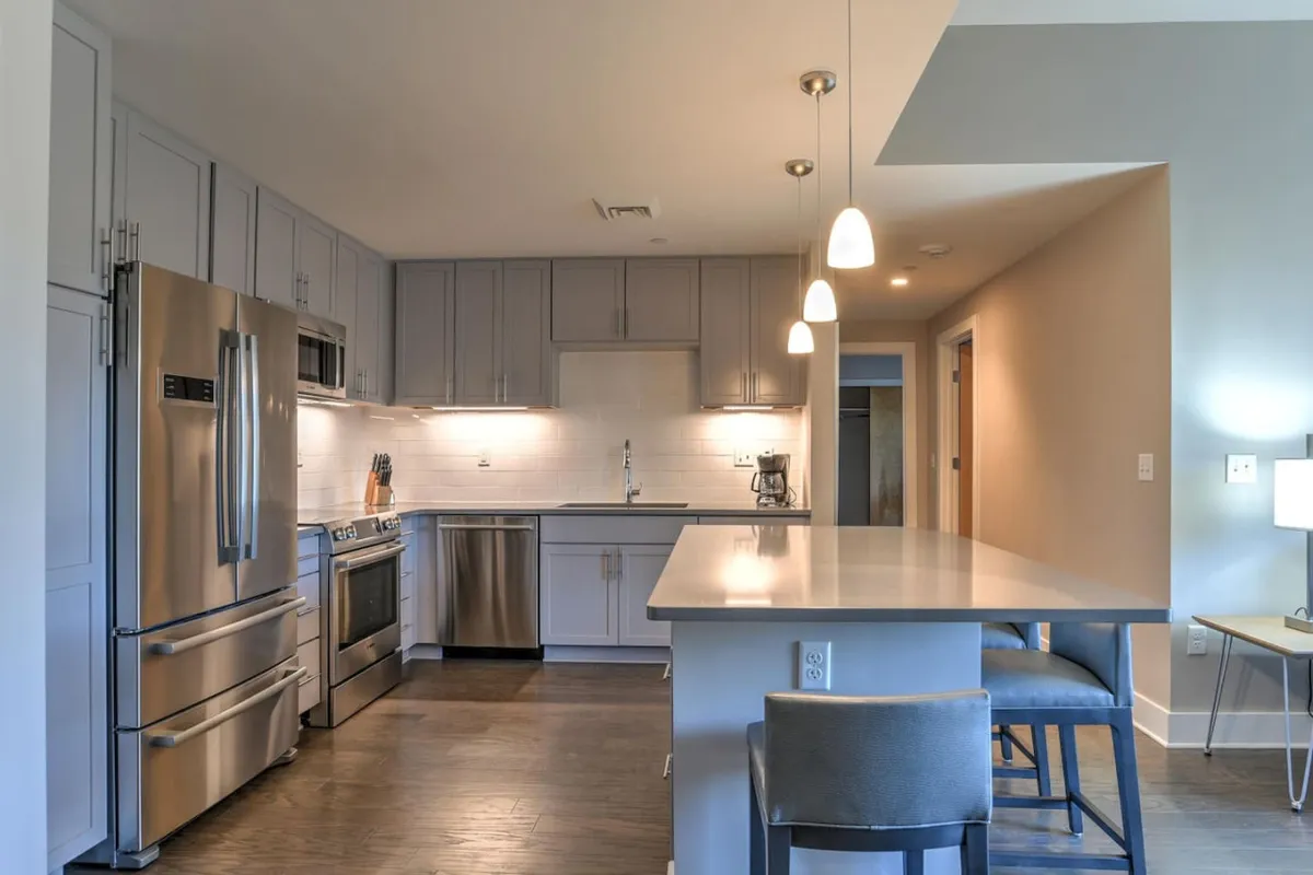 A modern kitchen featuring stainless steel appliances, a spacious kitchen island, and stylish pendant lighting. The setting is designed for cooking, entertaining, and casual dining, with ample space for guests to gather and share meals.