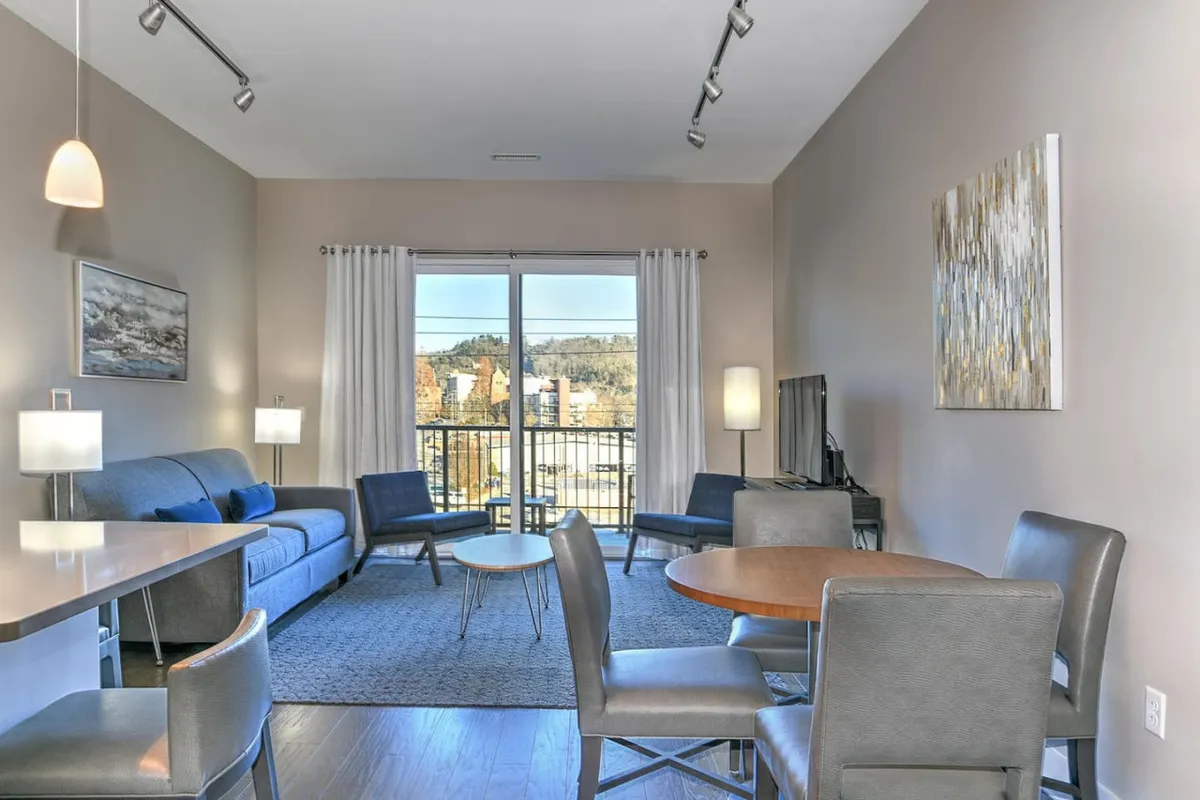 A spacious open-concept living and dining area bathed in natural light from large windows. A comfortable sofa and modern dining table invite relaxation and social gatherings, while tasteful artwork adds personality. The scene captures casual moments like relaxing, dining, and socializing in a space designed for connection.