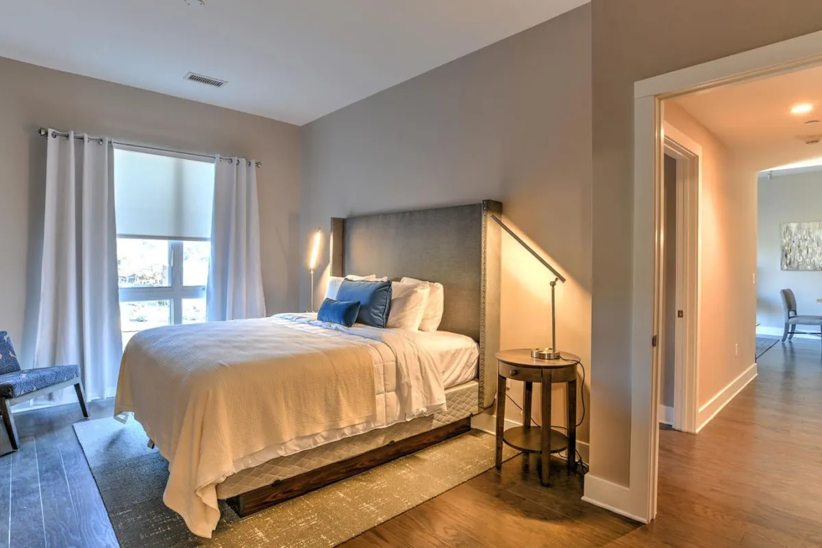 Another tranquil bedroom with a bed, nightstand, lamp, cozy chair, and window letting in natural light. The setup highlights both comfort and functionality, ideal for unwinding after a day in the city.