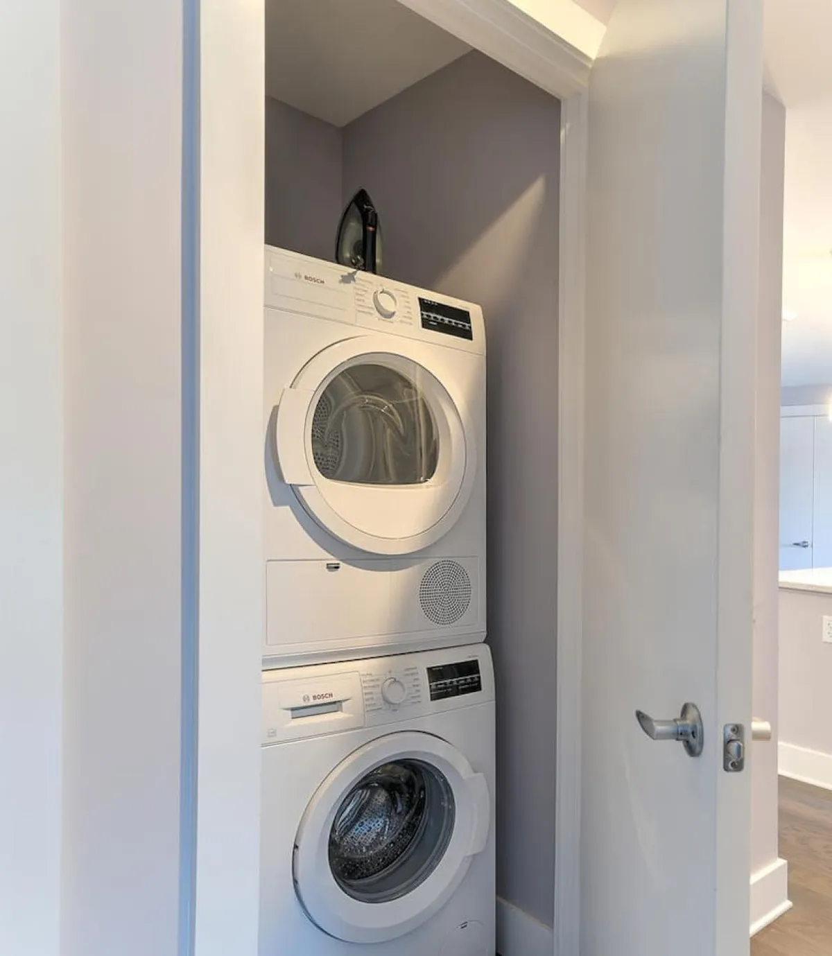 A practical interior view featuring a stacked washer and dryer unit with an iron placed on top. The laundry area is clean and organized, underscoring the efficiency and attention to detail present throughout the property.